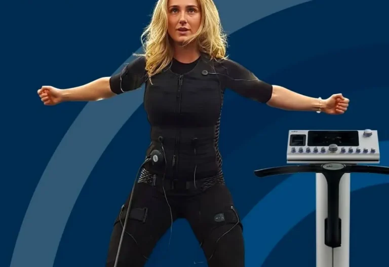 Vrouw in een zwart EMS-trainingspak met gespreide armen naast een miha bodytec-toestel