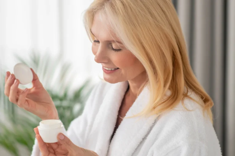 Vrouw in een witte badjas opent een pot crème