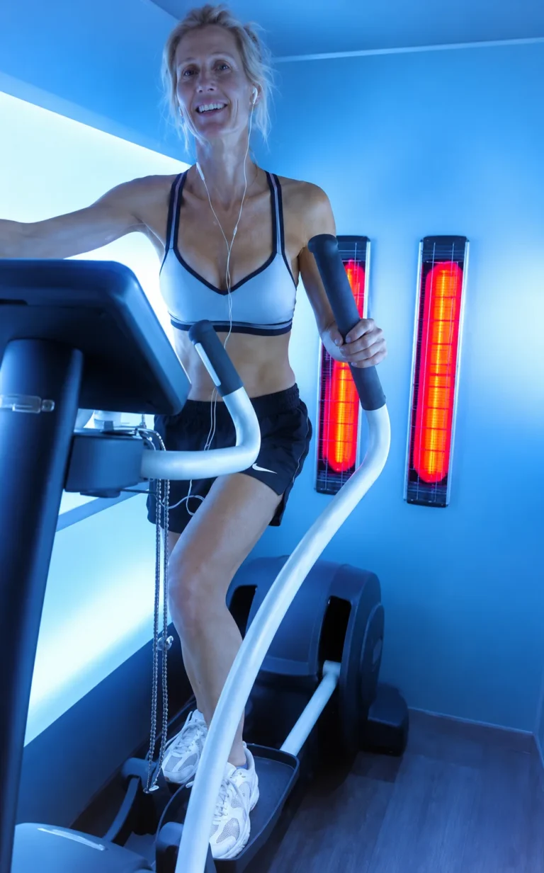Een vrouw traint lachend op de crosstrainer in de lichtbox met infraroodlampen