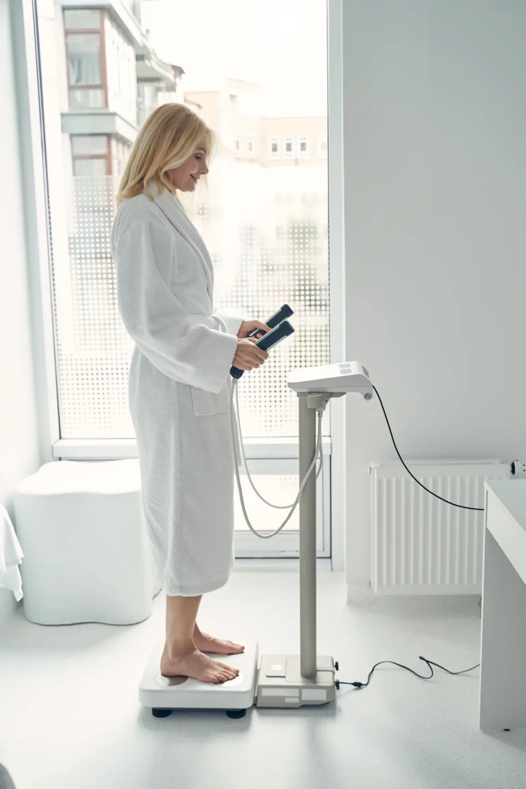 Vrouw in een badjas staat op een toestel voor lichaamsanalyse met de handgrepen vast