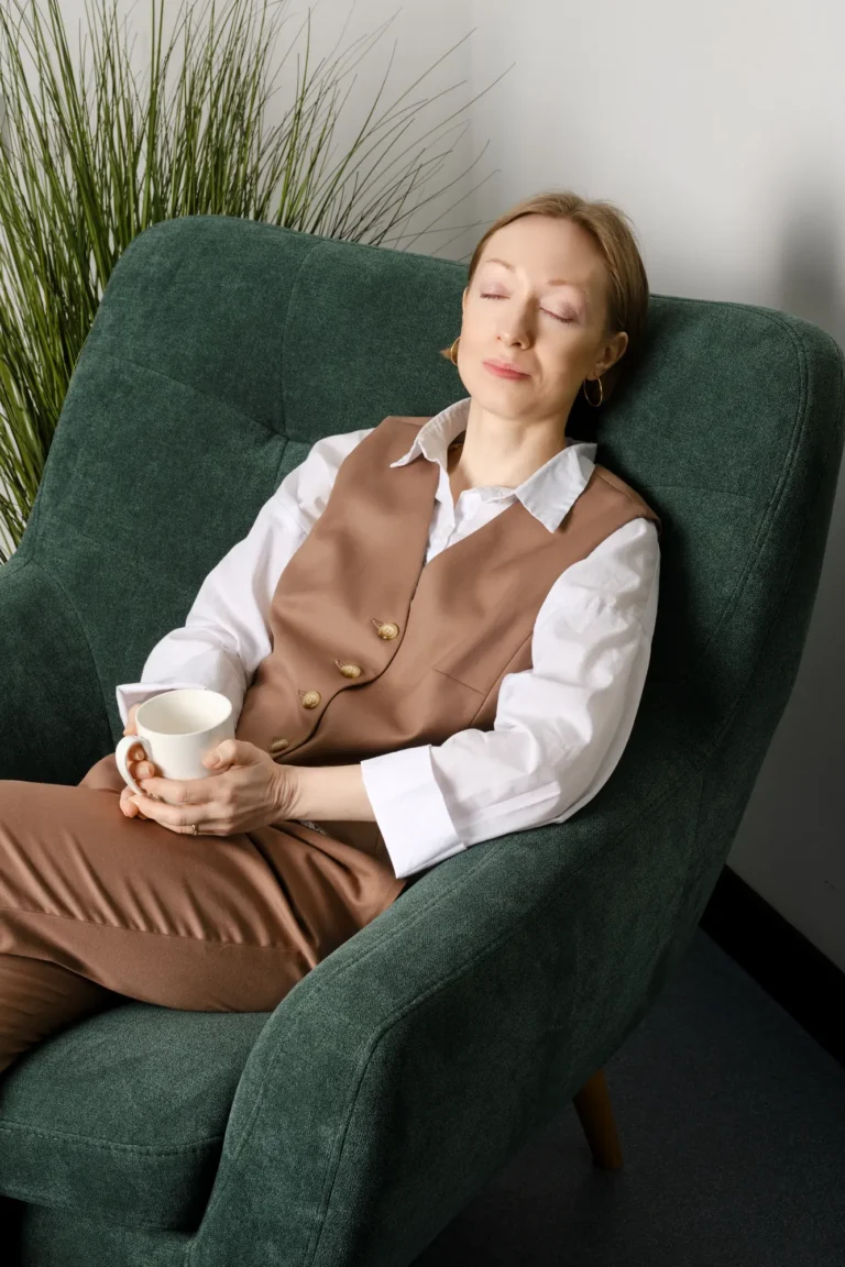 Vrouw ontspant met gesloten ogen en een kop thee in een groene fauteuil