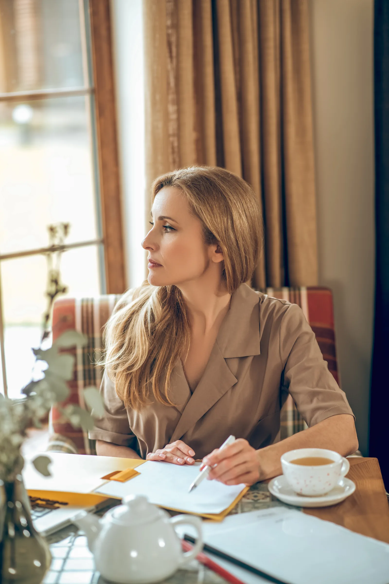 Vrouw schrijft in een notitieboek aan tafel met een kop thee en kijkt opzij