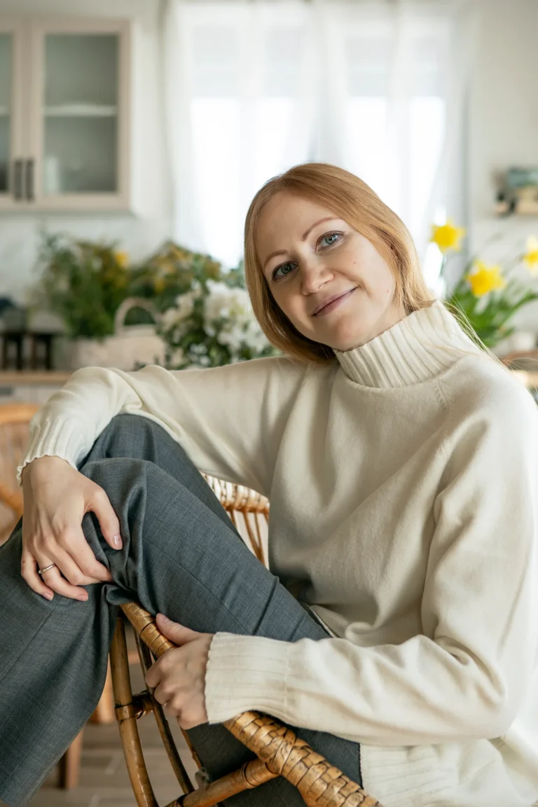 Vrouw van middelbare leeftijd in een crème trui ontspant in een rieten stoel bij het raam